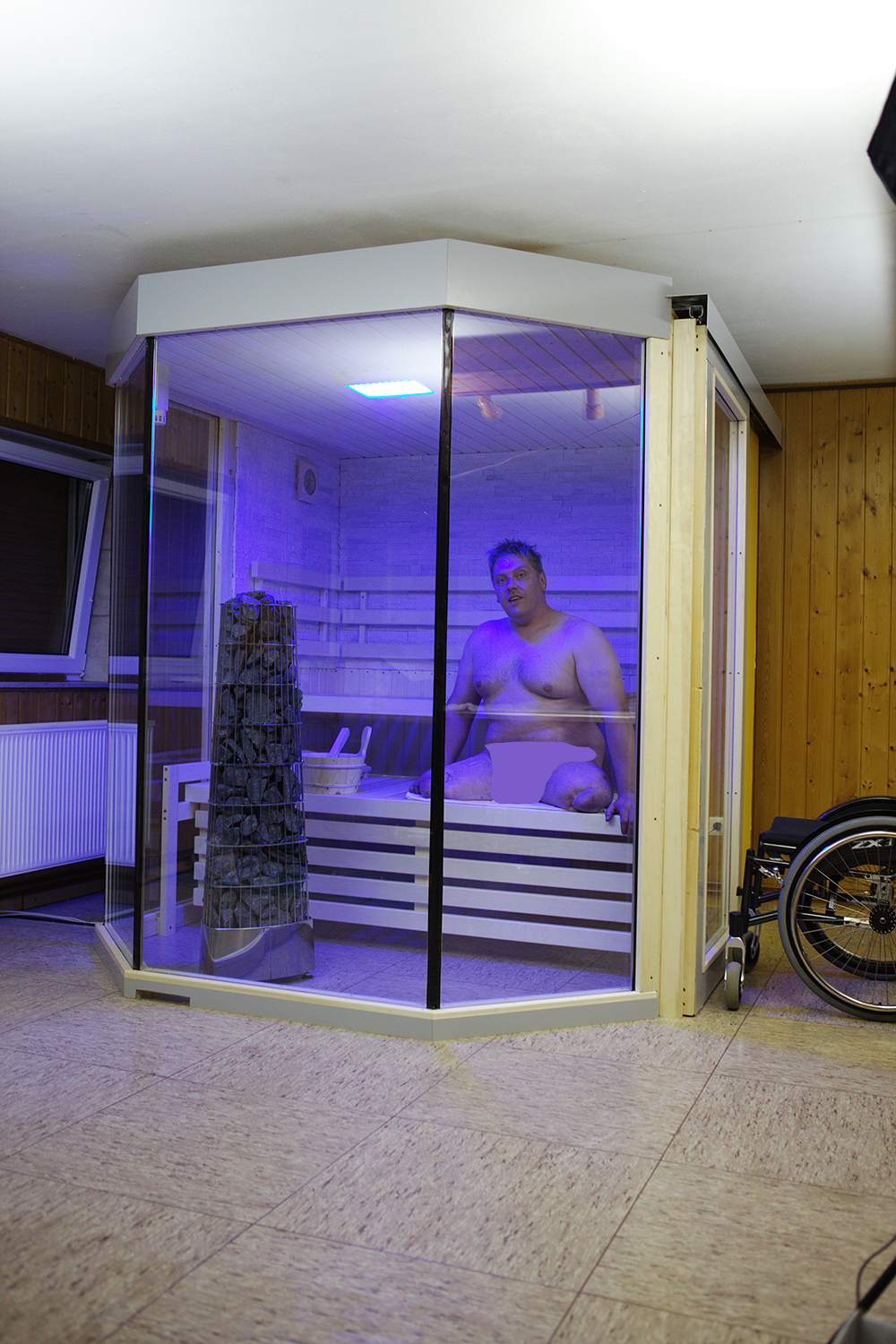 Gesamtansicht der barrierefreien Heimsauna mit Glasfront, geöffneter Schiebetür und Rollstuhl daneben
