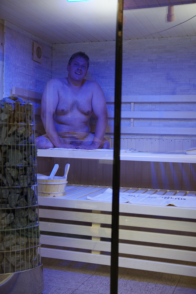Innenansicht der Heimsauna mit Person auf der Saunabank, Ofen und barrierefreiem Raumkonzept